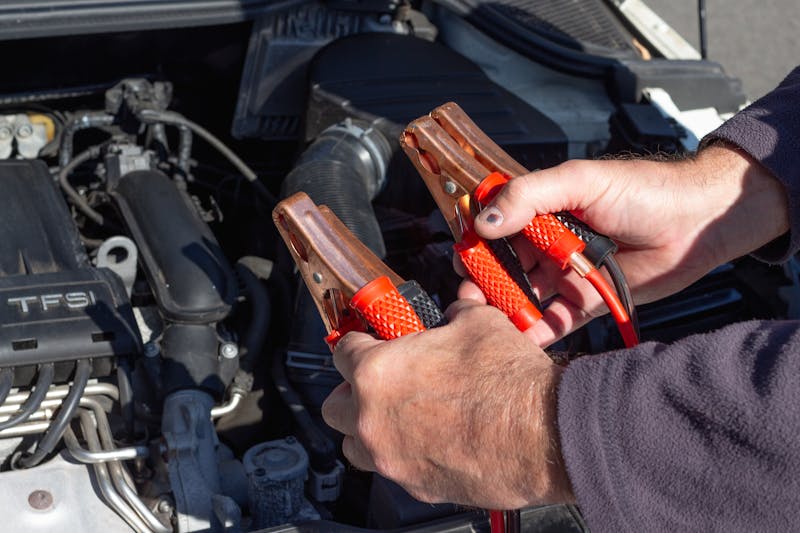Mechanic holding jumper cables near engine bay during mobile battery service